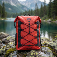 RIXVA 35L waterproof red PVC backpack with roll-top closure and front elastic bungee storage on a mossy rock by a lake.